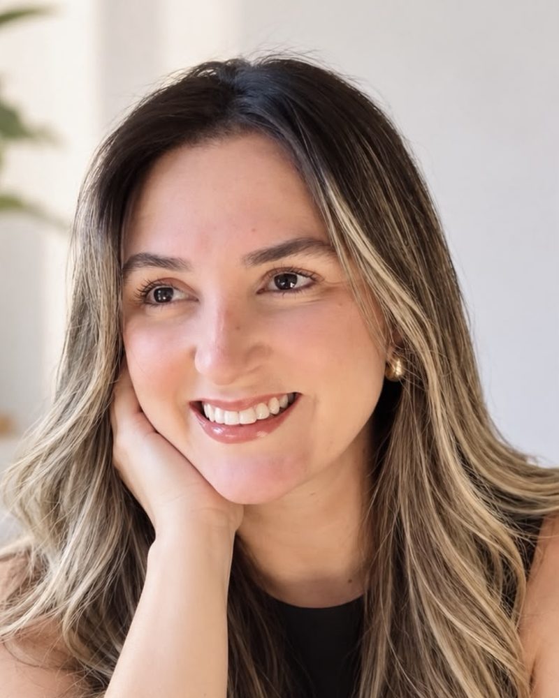 Thaynara Gomes sorrindo, com a mão apoiada no rosto